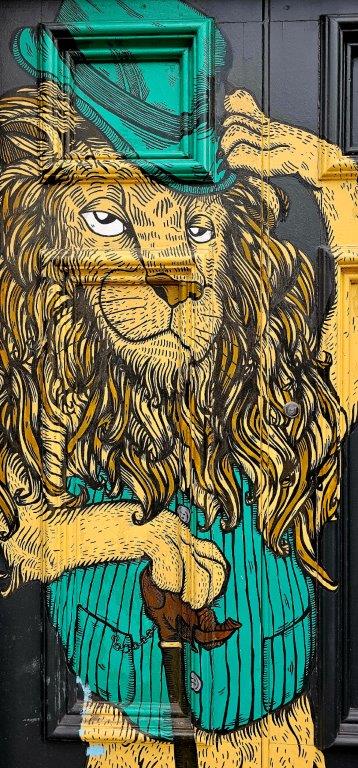 Lion in a top hat and striped waistcoat leaning on a cane, painted by Lucas Antics on a front door