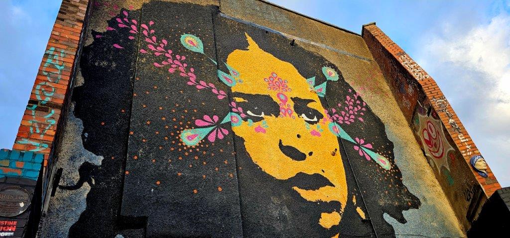 Giant stencilled portrait of a woman in yellow and black with pink and teal decoration, seen from below