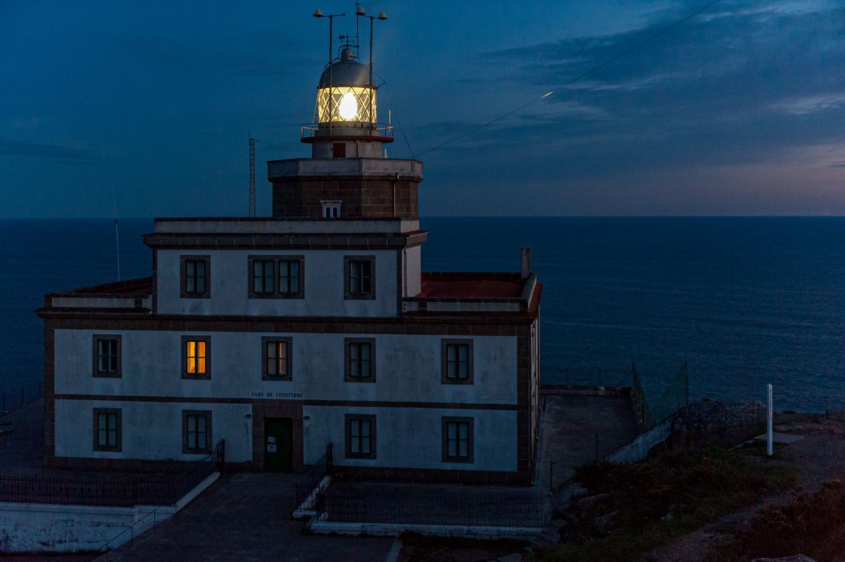 The lighthouse at Cape Finisterre in Galicia lit up at dusk