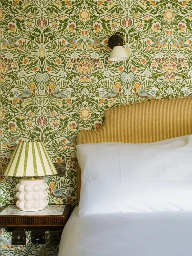 Bedroom with patterned wallpaper, padded headboard and bedside lamp at The Mason’s Arms, a Cotswolds inn in Clanfield
