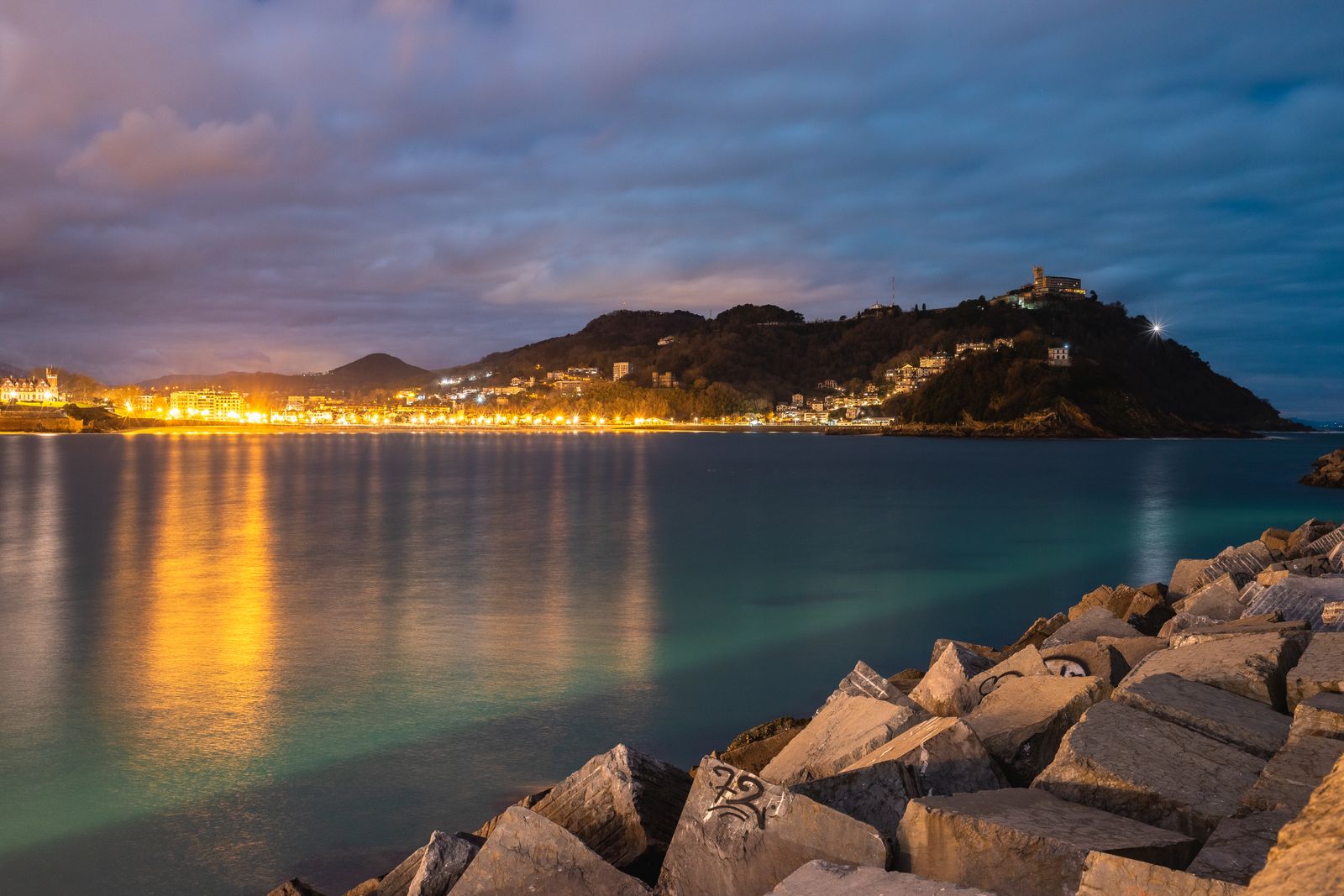 The coast of San Sebastian at dusk, with town lights reflected in the bay